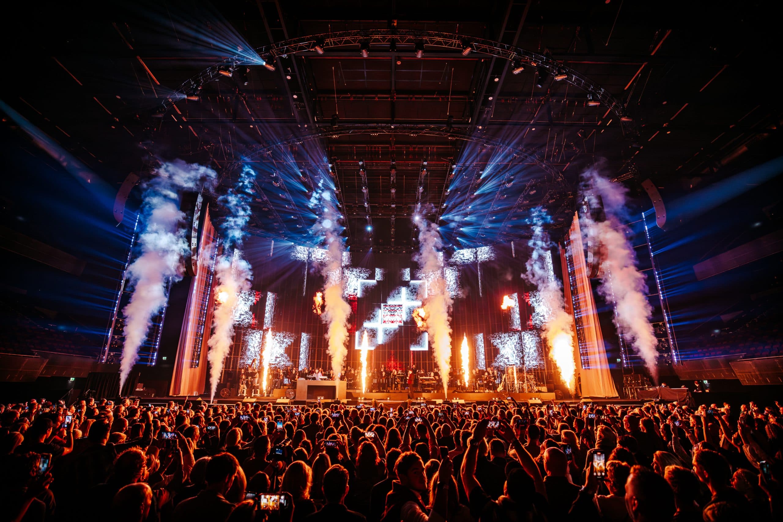 Concert audience facing a monumental stage composition lit with warm beams and video