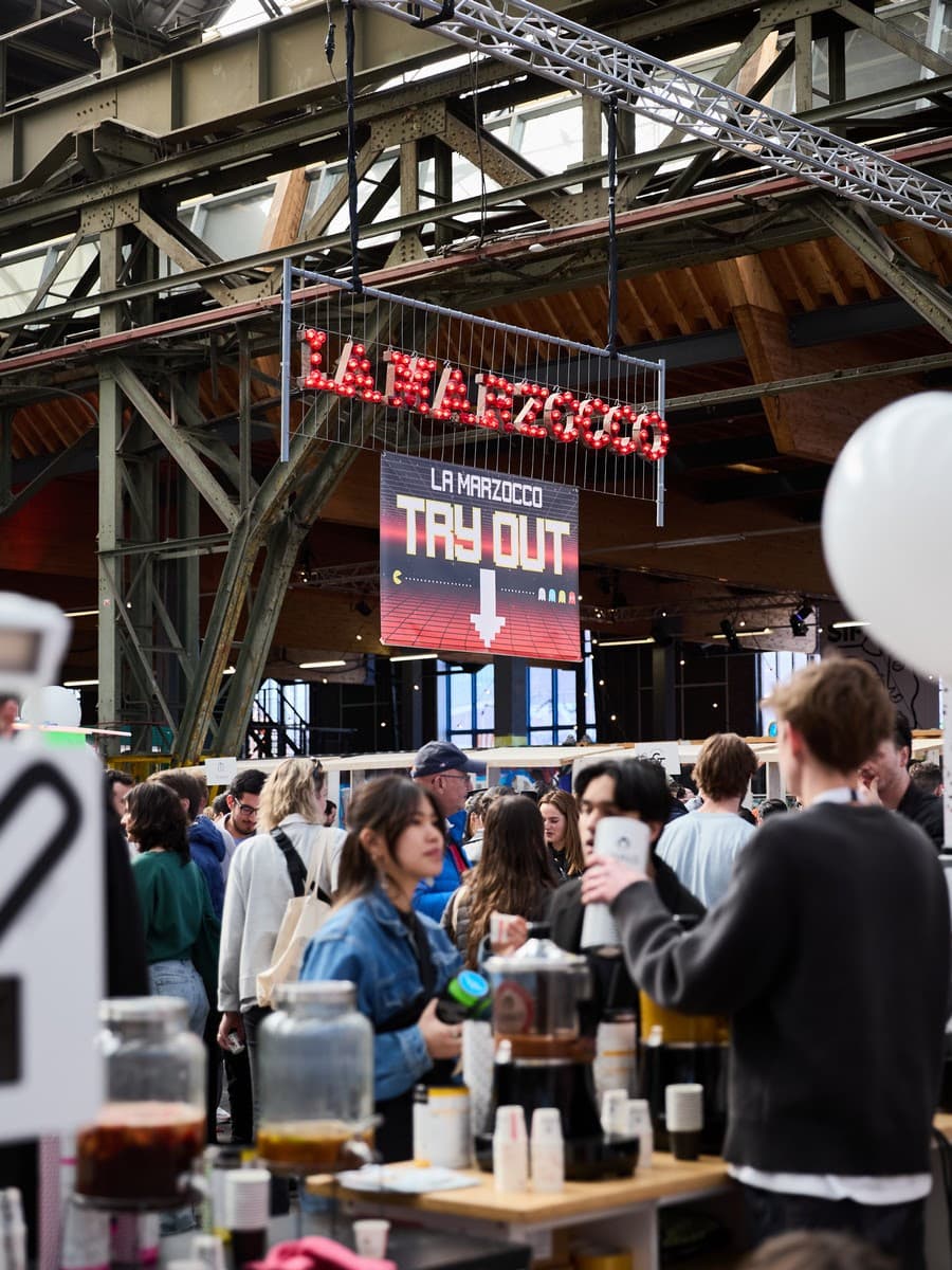 Busy festival floor with visitors, coffee stands and the La Marzocco sign inside NDSM
