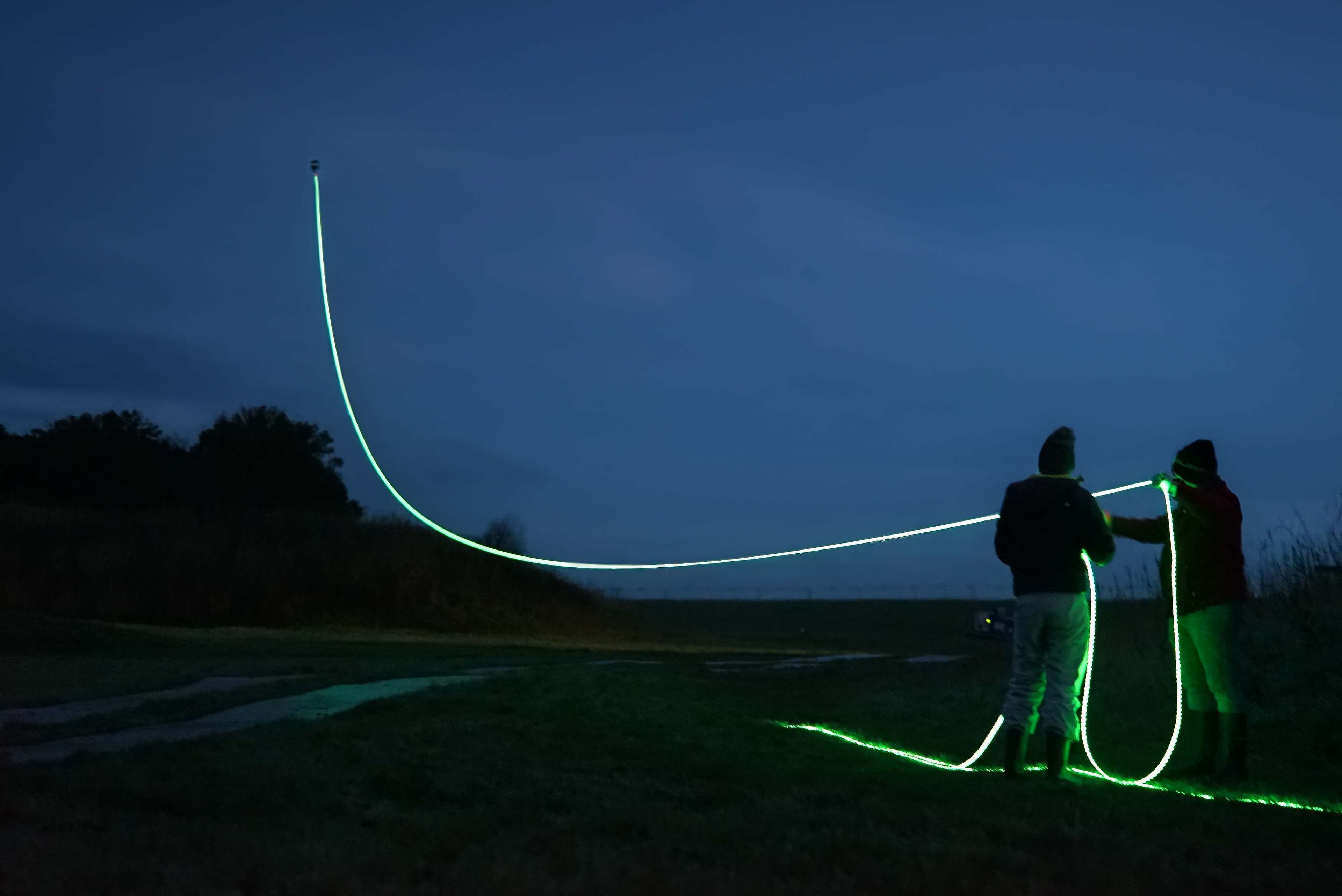 Windvogel kites drawing lines of green light across the night sky above a field