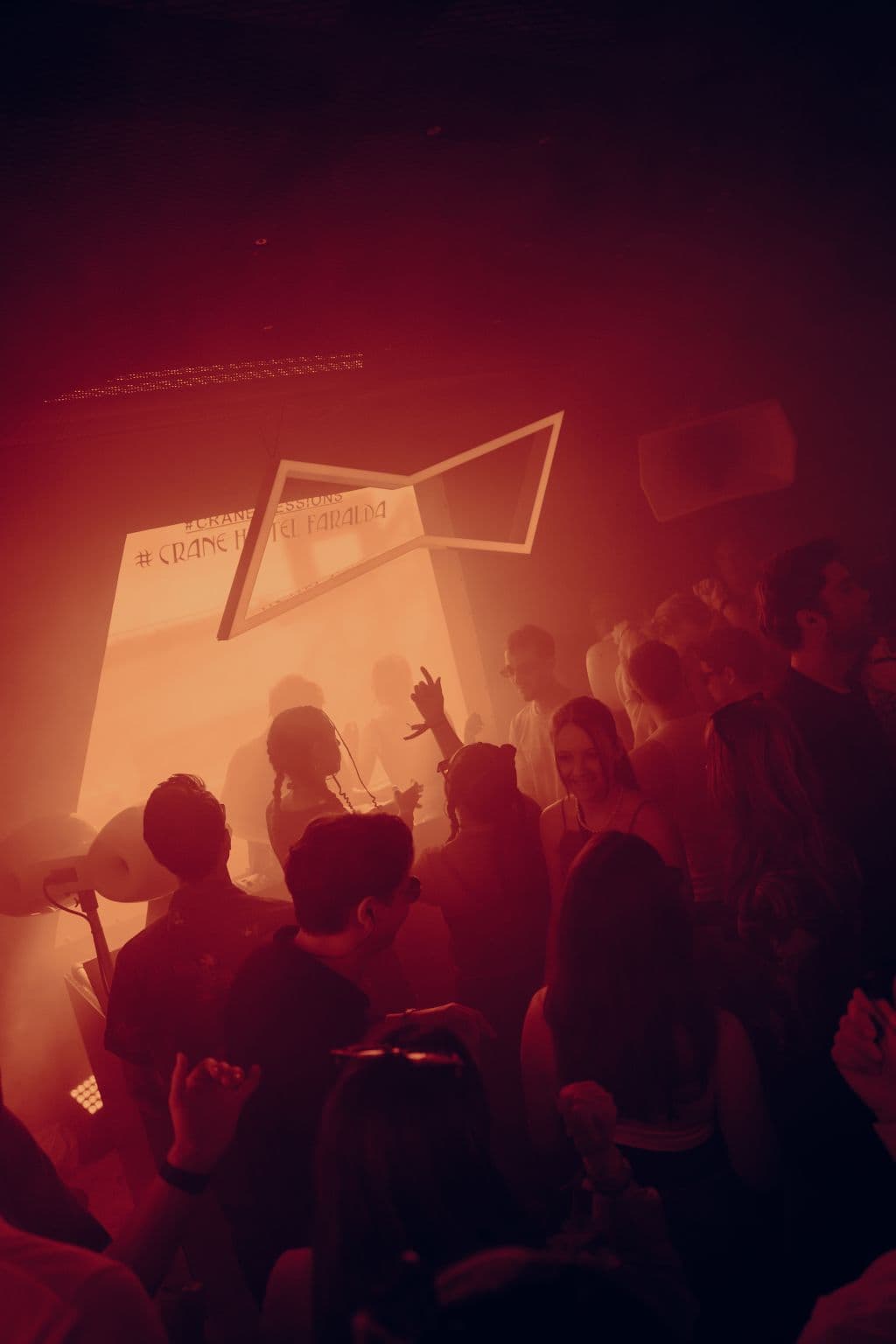 Dense festival crowd dancing in warm red light inside the BUD stage