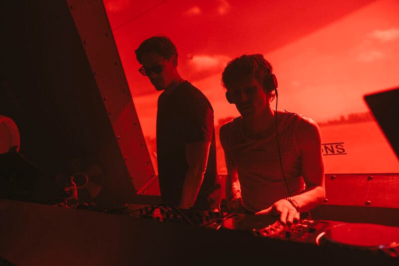 Two DJs performing beneath red light inside the BUD mini stage in the NDSM crane