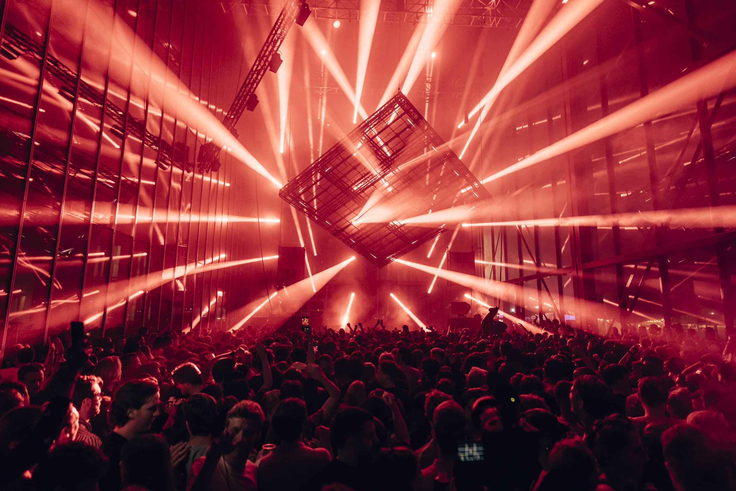 Audio Obscura at Amsterdam Dance Event: a rotated truss cube hanging in red laser light above a packed crowd