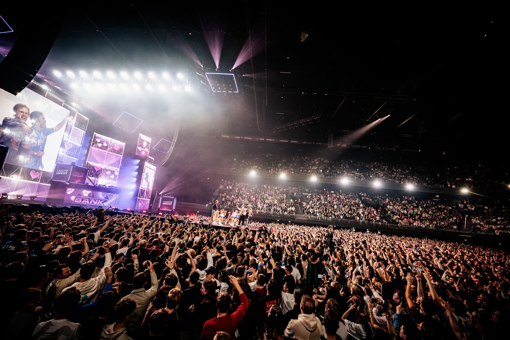 Bankzitters performing on a wide Ziggo Dome stage surrounded by blue light and screens