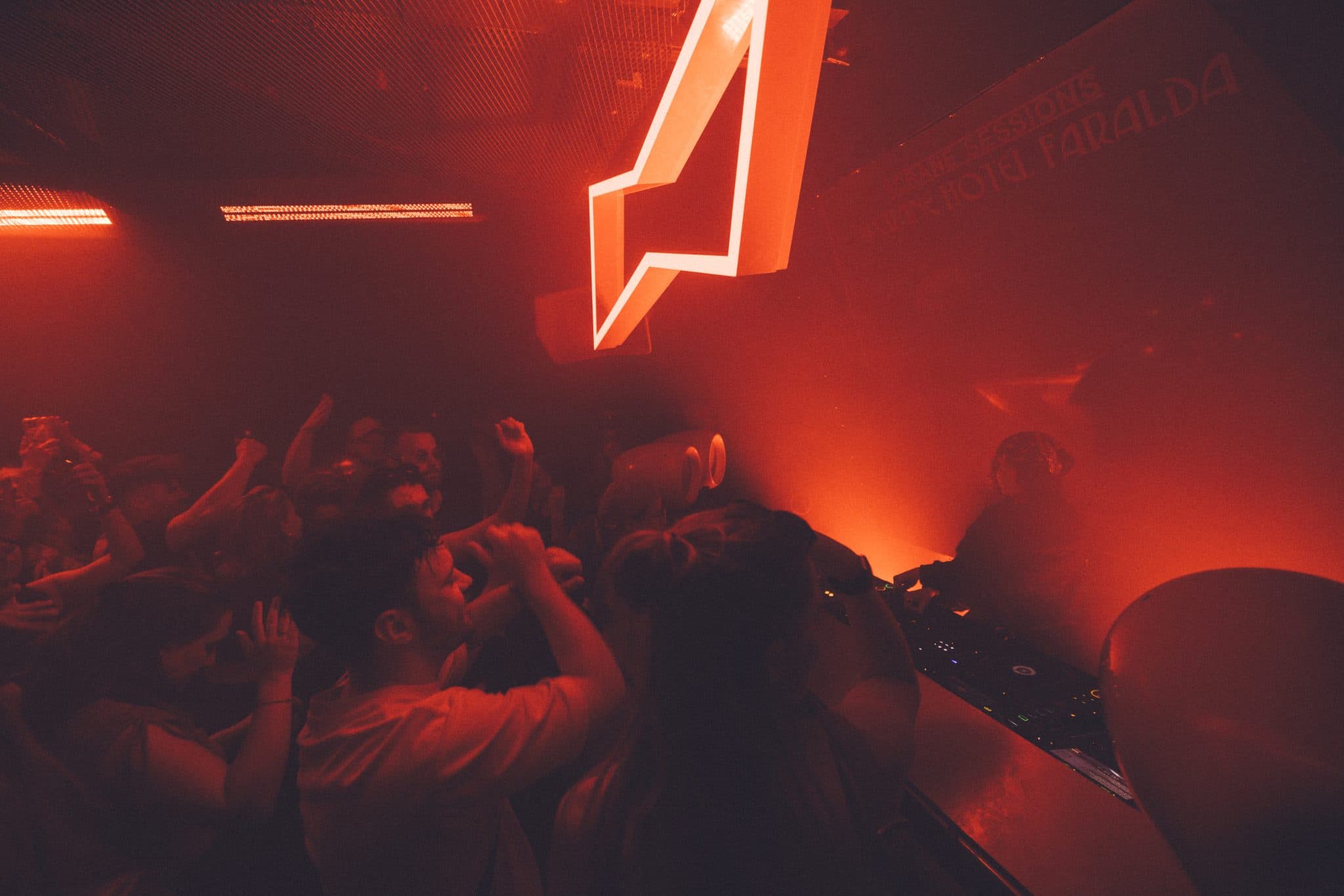 BUD × DGTL: crowd under a neon arrow mark in deep red club light and haze