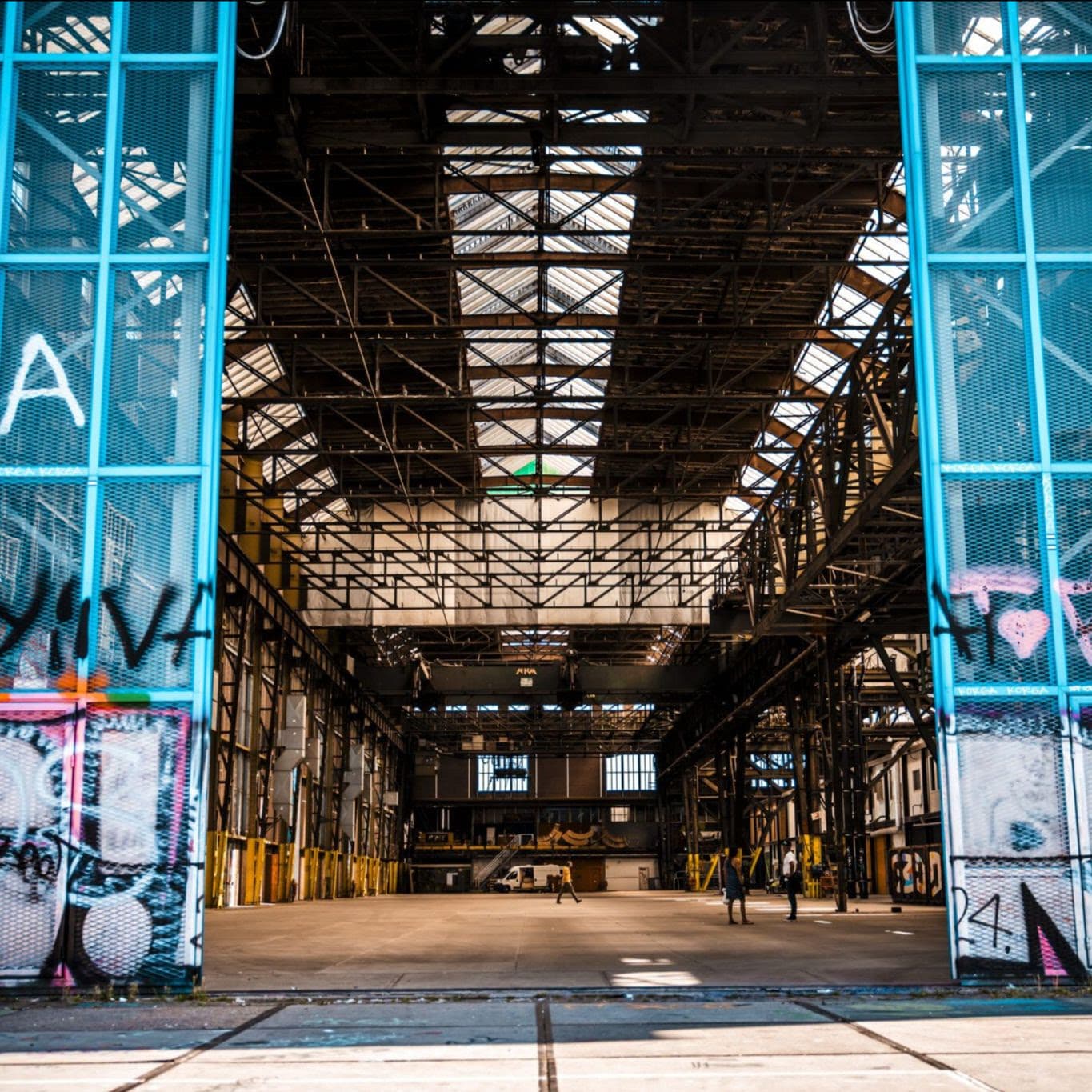 View through graffiti-covered blue doors into the empty NDSM warehouse under a long roof skylight