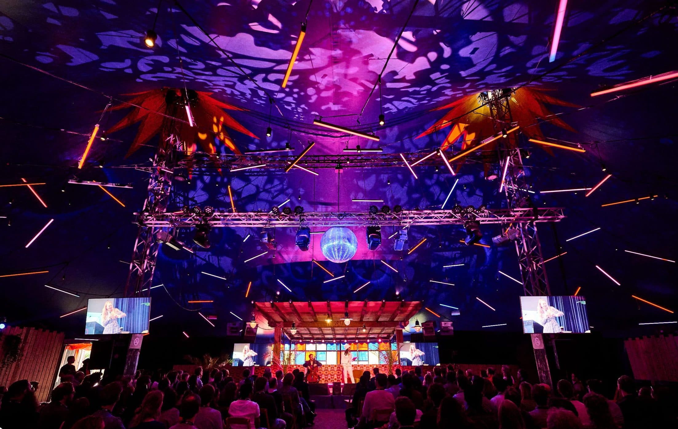 Conference tent with geometric truss, tube lights and a mirror ball above the audience