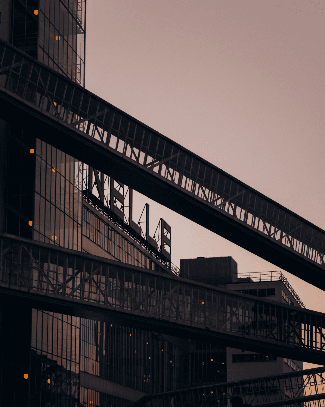 Glazed skybridges crossing between the dark Van Nelle Fabriek buildings against a dusk sky